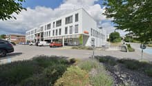 Modern multi-story building with white facade and large windows, featuring a colorful striped awning and signage for "Micros".