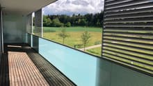 Modern balcony with wooden decking, glass railing, and scenic countryside view.