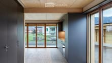 Open-plan unfurnished space with wooden ceiling and floor, large glass doors leading to outdoor view, grey walls, and minimal built-in cabinetry.