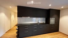 modern kitchen with black cabinets, wooden floor, black countertop, sink, faucet, integrated oven
