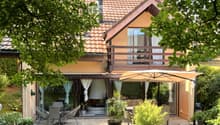 Garden area with a patio, outdoor furniture, umbrella, and a view of the house with a balcony and large windows.