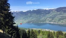 Panoramic view of a serene lake surrounded by lush green forests and snow-capped mountains under a clear blue sky.