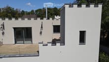 Modern two-story house with white exterior, crenellated roofline, large windows, and a balcony area with wooden decking.