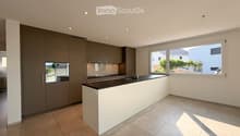 Modern kitchen with grey cabinetry, white island, black countertop, and stainless steel sink.