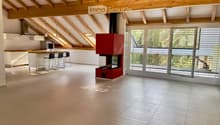 Open-plan living and kitchen area with exposed wooden beams, a modern fireplace, and large sliding glass doors leading to a balcony.