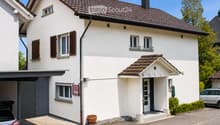 Two-story white house with a tiled roof, multiple windows with shutters, a garage, and a small entrance porch.