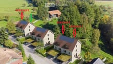 Aerial view of a residential area with multiple houses, green lawns, trees, and driveways. Some houses have solar panels on the roofs.