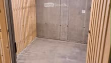Empty room with unfinished concrete walls and floor, wooden framing on the sides, and exposed ductwork on the ceiling.