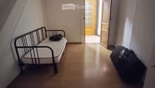 A small, furnished room with a single bed, a suitcase, and an open doorway leading to another room.