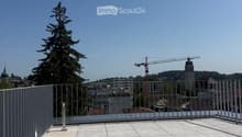 Roof terrace with modern metal railing, tiled floor, and a view of the city skyline, trees, and a construction crane.
