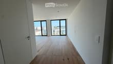 Empty hallway with wooden flooring, white walls, and large windows at the end leading to an outdoor area.