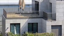 Modern building with grey facade, large windows, and balconies featuring metal railings and closed umbrellas.