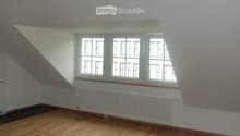 Empty room with wooden flooring, white walls, and large windows with white frames. A radiator is visible below the windows.