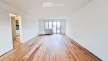 Empty room with wooden flooring, white walls, and large glass doors leading to a balcony.