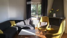 Modern living room with a grey sectional sofa, yellow chairs, a white coffee table, and a fireplace with a vase of sunflowers on the mantel.