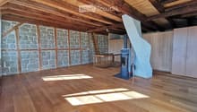 Empty room with wooden flooring, exposed wooden beams, stone walls, and a staircase leading to an upper level. No furniture or equipment is present.