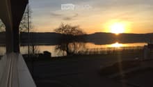 Balcony overlooking a serene lake at sunset, with trees and distant hills visible.