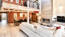 Open-plan living and dining area with a white sectional sofa, coffee table, fireplace, TV, dining table with chairs, and a wooden cabinet.