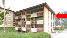 Multi-story apartment building with balconies and large windows, surrounded by greenery and mountains.