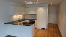 Modern kitchen with white cabinets, black countertop, built-in sink, and oven. Wooden flooring and recessed lighting.