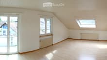 Empty attic room with wooden flooring, white walls, large windows, and a skylight. No furniture or equipment present.