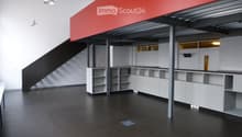 Open-plan unfurnished space with white walls, black floor, white shelving units, and a staircase leading to an upper level.