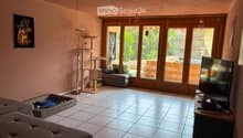 Living room with tiled floor, large windows, cat tree, sofa, television, and a stool.