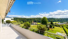 Balcony with tiled floor, metal railing, overlooking a green park area with trees, a playground, and distant mountains.