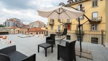Roof terrace with tiled floor, metal railing, and outdoor furniture including chairs, a table, and a large umbrella.