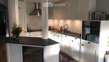 Modern kitchen with white cabinets, black countertops, stainless steel appliances, and a central island. Features a sink, faucet, and decorative vase on the counter.