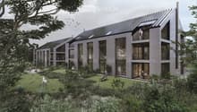 A modern, multi-story building with a slanted roof and large windows, surrounded by a lush, green landscape with trees and vegetation. The building appears to have balconies or terraces on some floors.