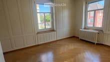 Empty room with wooden flooring, white walls, and two windows with radiators beneath them.