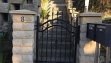 Stone entrance pillars, black wrought iron gate, stone walkway, metal handrails, stone steps, mailboxes on right, number 8 on left pillar.