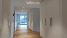 Modern hallway with light wooden flooring, white walls, built-in storage units, and recessed lighting.