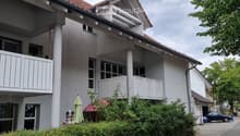 Two-story residential building with white exterior, multiple windows, balconies, and a well-maintained garden area.