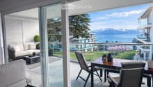 Balcony with a view of a lake and mountains, featuring a sofa, coffee table, and outdoor dining set.