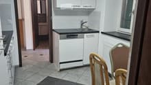 Modern kitchen with white cabinets, a dishwasher, sink, and two wooden chairs near the window.