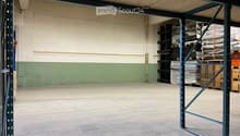 Empty warehouse space with concrete floor, metal shelving units, and storage crates in the background.