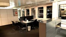 Modern office space with desks, chairs, computers, and large windows overlooking the city.