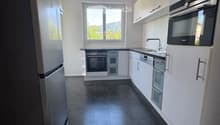 Modern kitchen with white cabinets, stainless steel appliances, dark tiled floor, and a window offering a view of greenery.