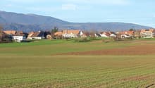 Rural landscape with scattered houses, green fields, and distant mountains under a clear sky.