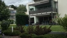 Modern two-story house with white exterior, large windows, balcony, and well-maintained garden.