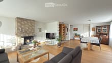 Bright living room with wooden flooring, a dark grey sofa, a glass coffee table, a fireplace with candles, a TV stand, a dining area with a table and chairs, and a wooden cabinet.