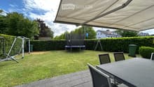 Backyard with a trampoline, swing set, patio furniture, and covered seating area.