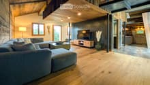 Modern living room with wooden floors, exposed wooden beams, large windows, sectional sofa, coffee table, TV, and decorative vase.