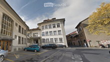 Urban street view with multi-story buildings, parked cars, and a clear sky.