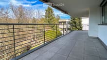 Balcony with tiled floor, metal railing, and a view of trees and a building in the background.