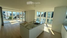 Modern kitchen with light wooden flooring, white cabinets, marble countertop, and large windows offering a view of the city.