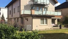 2-story residential building with beige exterior, red tile roof, balconies, and a fenced yard with vegetation.