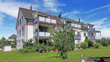 Modern multi-story residential building with balconies, surrounded by a well-maintained lawn and garden area.